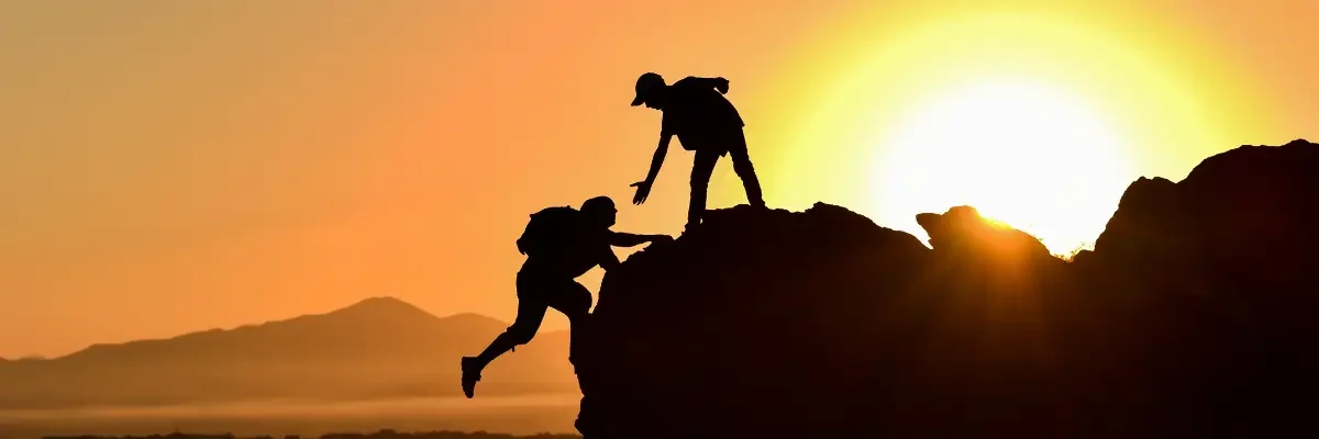 Accompagnement doux et personnalisé, personne tendant la main à une autre escaladant une montagne.